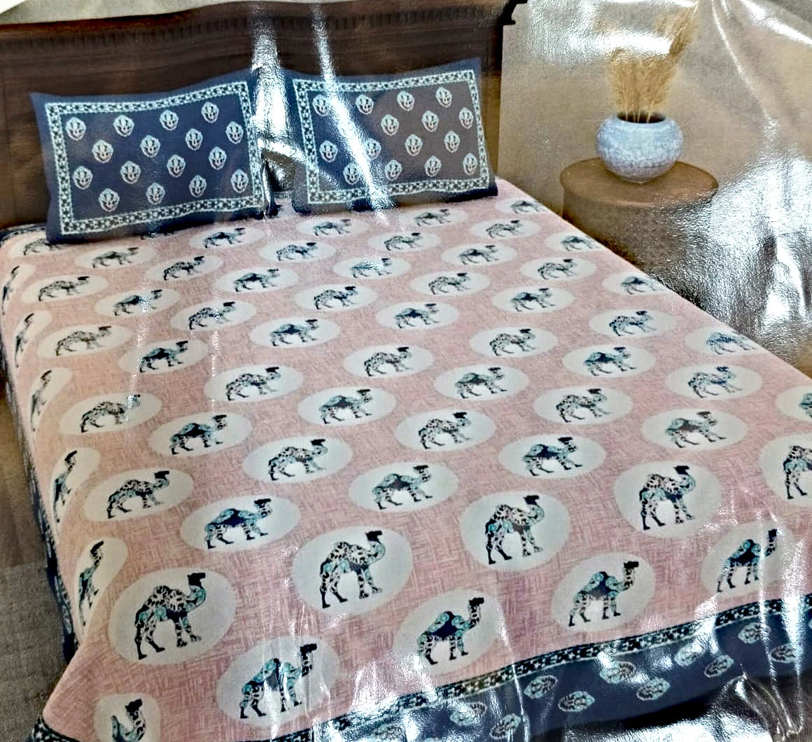 The Camels: camels in cream roundels on blush pink, with blue paisley pillowcases, on a made bed with matching pillowcases.