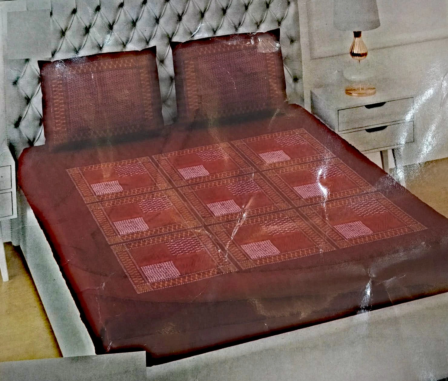 The Crimson: deep maroon with fine geometric panels in rose and cream, on a made bed with matching pillowcases.