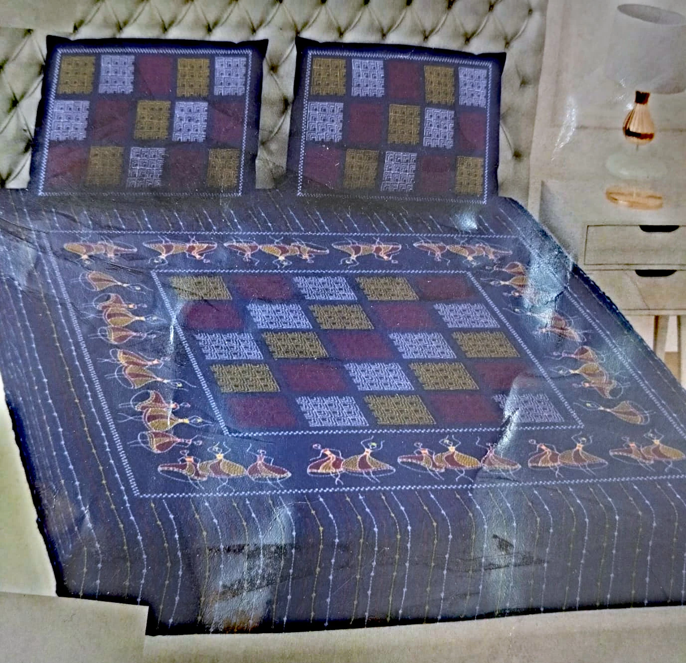 The Dancers, navy: dancing figures and square panels in ochre, rose and white on navy cotton, on a made bed with matching pillowcases.