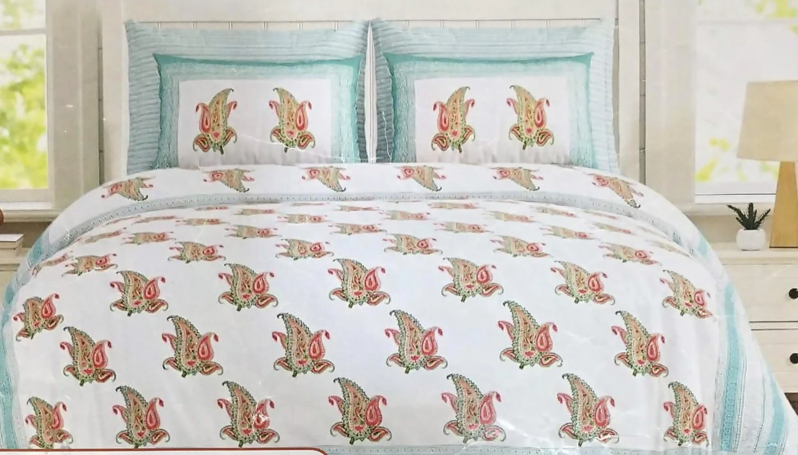 The Paisley, white: rose and green paisley on white cotton with a teal border, on a made bed with matching pillowcases.