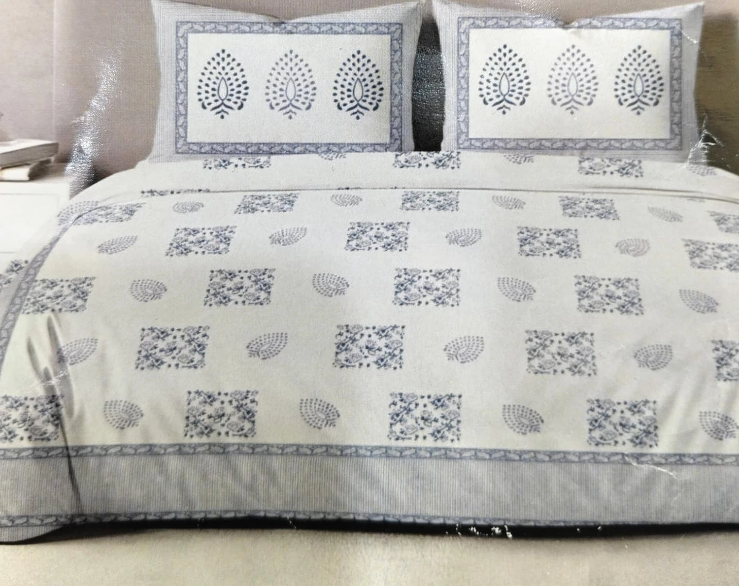 The Silverleaf: large grey leaf motifs on white with a patterned grey border, on a made bed with matching pillowcases.